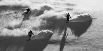 Drei Skiläufer in voller Ausrüstung fahren mit hoher Geschwindigkeit den Hang hinunter, während der Schnee unter seinen Skiern aufwirbelt.