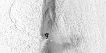 Ein Skifahrer stürzt sich wagemutig eine steile Abfahrt in Zermatt hinunter, umgeben von tief verschneiten Hängen.