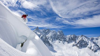Ein Skifahrer stürzt sich wagemutig eine steile Abfahrt in Zermatt hinunter, umgeben von tief verschneiten Hängen und imposanten Bergspitzen.