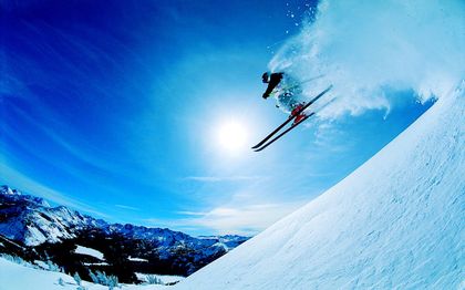 Ein Skiläufer in voller Ausrüstung fährt mit hoher Geschwindigkeit den Hang hinunter, während der Schnee unter seinen Skiern aufwirbelt.