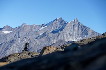 Auf einem steilen Anstieg in Zermatt strampelt ein Mountainbiker entschlossen weiter, während die Alpen im Hintergrund aufragen.