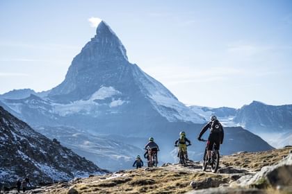 Eine Gruppe von Mountainbikern kämpft sich tapfer über einen felsigen Trail in Zermatt, umgeben von unberührter Natur.