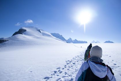 Eine Gruppe von Skitourengeherinnen und -geher erreicht den Gipfel eines hohen Berges in Zermatt und genießt das 360-Grad-Panorama der schneebedeckten Alpen.