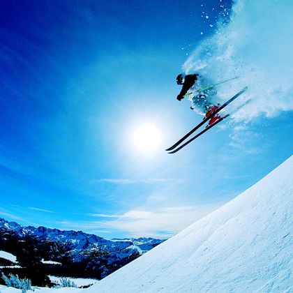 Ein Skiläufer in voller Ausrüstung fährt mit hoher Geschwindigkeit den Hang hinunter, während der Schnee unter seinen Skiern aufwirbelt.
